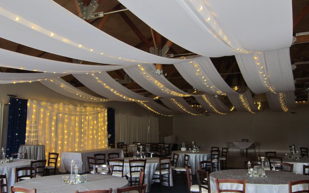 Wedding setup at Devonvale Wine Estate, Stellenbosch, featuring a white bridal backdrop with royal blue accents and ceiling strips of white fabric with fairy lights by The Events Draping Co.