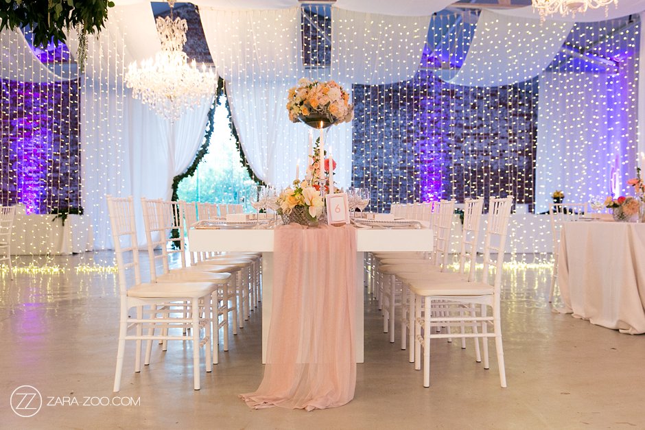 Elegant event setup with parallel white ceiling swags, draped entrance with opening, and a beautifully decorated table with floral centerpiece by The Events Draping Co.