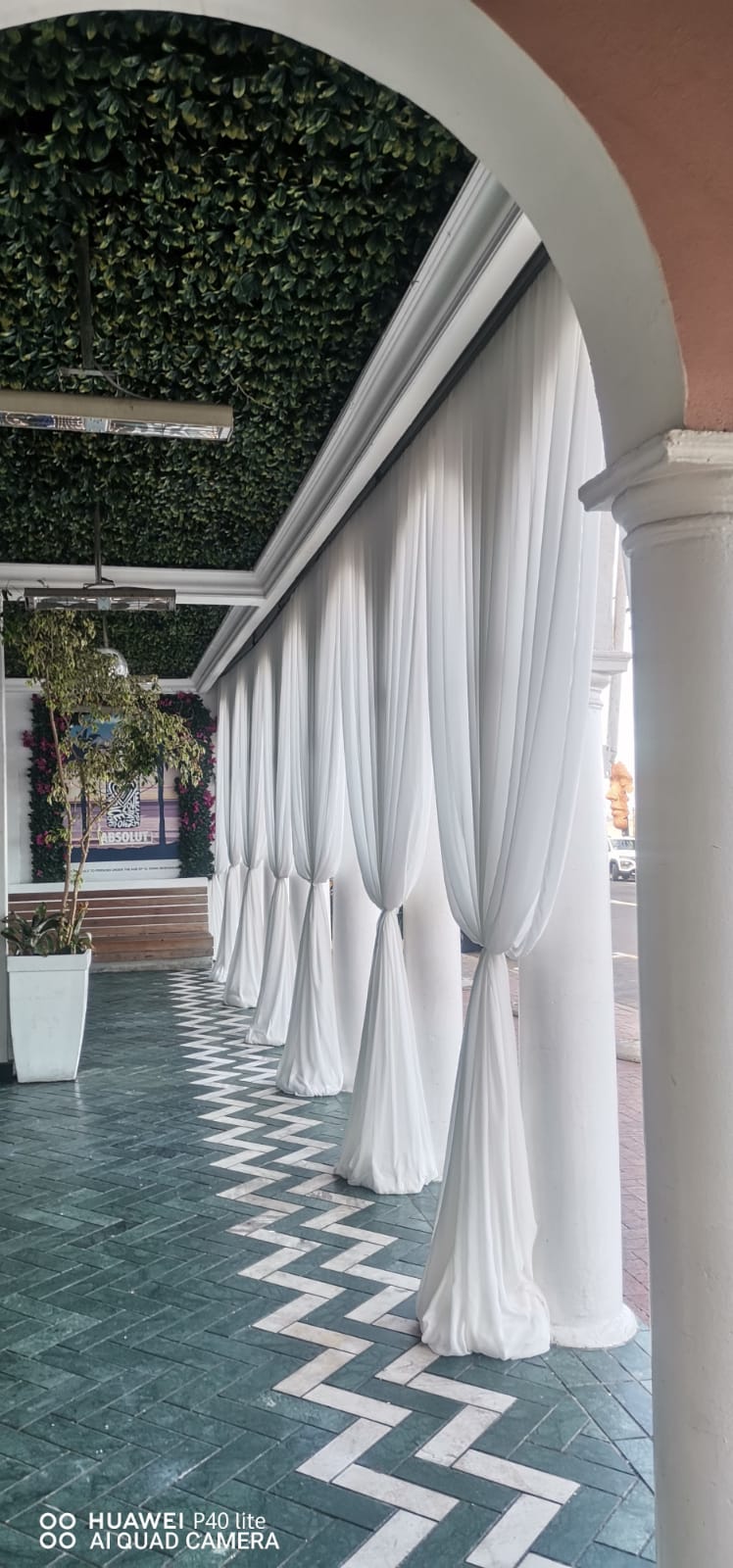 White chiffon tie-back draping swags at a series of pillars, creating a graceful and airy effect in an outdoor walkway, by The Events Draping Co.