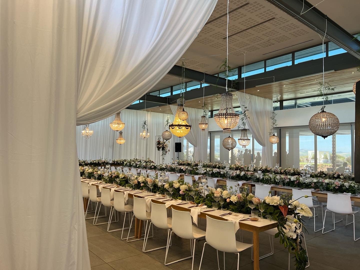 Series of side-facing white tieback draping swags for a wedding, featuring long banquet tables decorated with floral arrangements and hanging lanterns, created by The Events Draping Co.