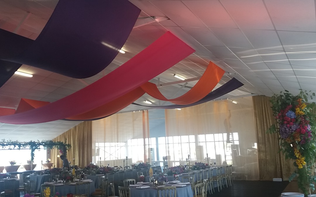 Pre-wedding Mehndi celebration at The Lookout, V&A Waterfront, featuring pink, orange, and purple ceiling strips, and a curtain of gold velour and mesh fabric by The Events Draping Co.