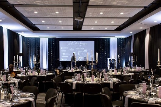 Black fabric with silver grey accents draped behind the stage and on the sides of the Century City Conference Centre for the SA Guide Dog Association's gala dinner, featuring fairy lights by The Events Draping Co.