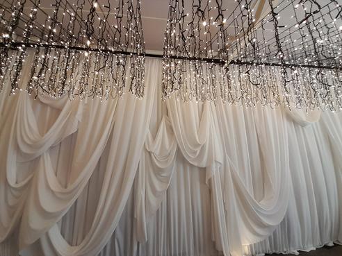White wall draping with random swag overlays and hanging fairy lights by The Events Draping Co.