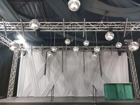 Criss-cross stage backdrop in white fabric by The Events Draping Co., enhancing the stage's visual appeal.